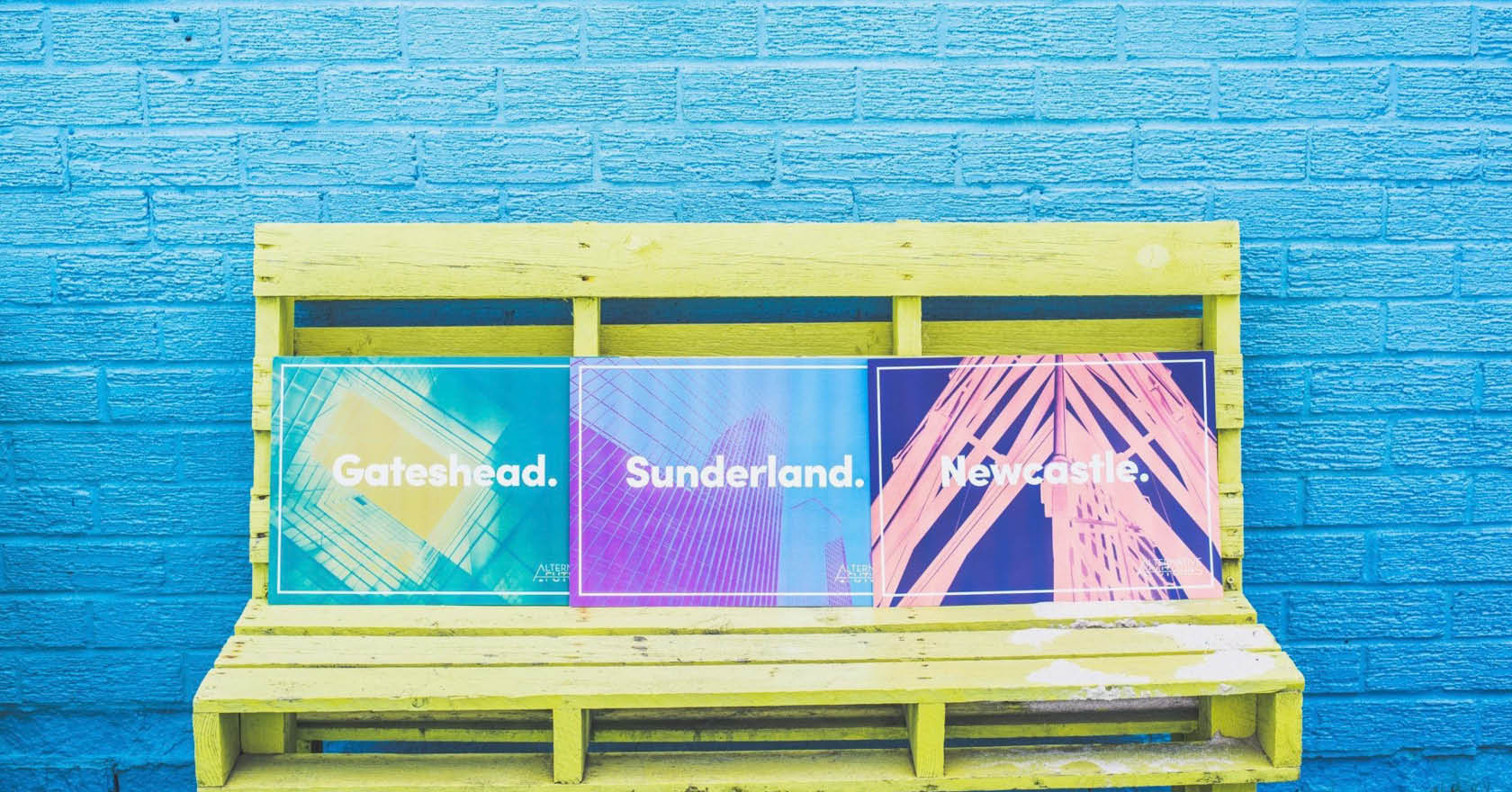 Three colourful posters from the Alternative Futures exhibition design by Swaddle Creative on a blue background