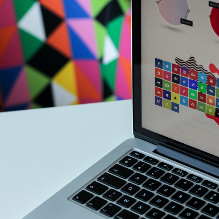 An open Mac laptop displays a colourful brand design, on a geometric background